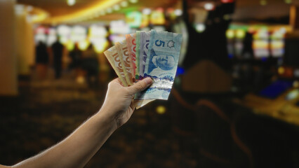 Man holding canadian dollars in a vibrant indoor casino with colorful slot machines, showcasing the...