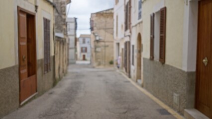 Fototapeta premium Blurred view of a narrow mediterranean street in an old town, featuring traditional rustic buildings with wooden doors and shutters, capturing a calm, nostalgic atmosphere.