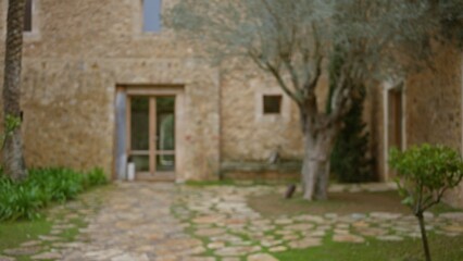 Blurred view of an old mediterranean stone house with a bokeh effect, featuring a rustic outdoor setting with trees and greenery in the foreground.