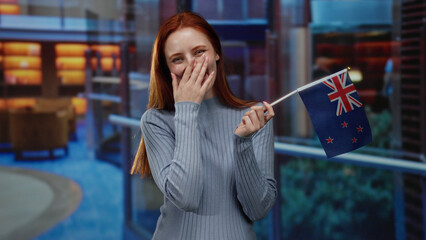 Woman holding new zealand flag indoors in hotel smiling with happiness showcasing patriotism and...