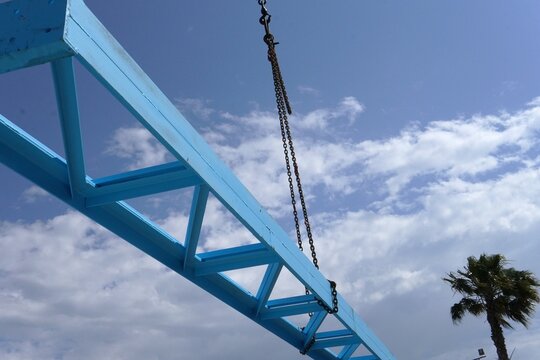 Assembling a steel structure. A construction site where a steel structure is being assembled. A crane with heavy chains. Scaffolding provides support for workers. Bright blue and industrial landscape.