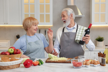 Senior man suggesting wine to his wife while cooking in kitchen