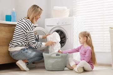 Mother and daughter with laundry basket loading washing machine together at home
