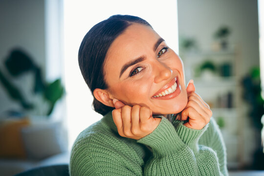 Smiling brunette woman in cozy green sweater enjoying her time indoors at a stylish home living area