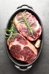 Pieces of raw beef meat and spices in baking dish on gray textured table, top view