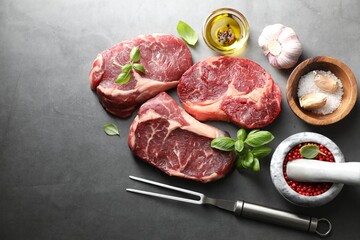 Pieces of raw beef meat, spices and carving fork on grey table, flat lay. Space for text