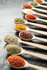 Many different spices in spoons on black table, closeup