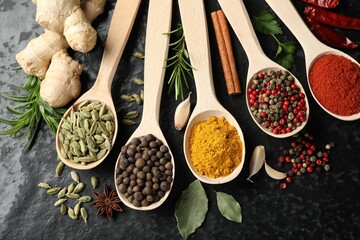 Many different spices in spoons on black table, flat lay
