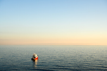 Evening coastal scene with lonely fishing boat in calm water of Mediterranean sea at sunset. Landscape photography