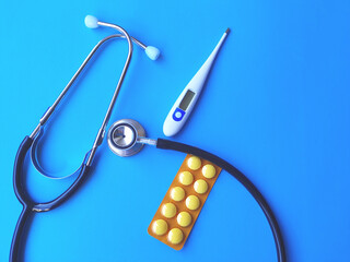 Stethoscope, pill and thermometer on blue background