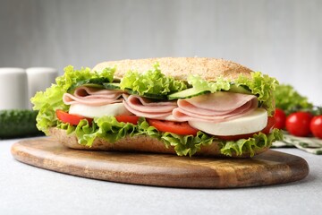 Tasty baguette sandwich with ham and vegetables on light grey table, closeup
