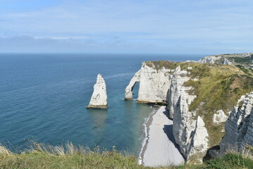 Plage et falaises d'Étretat, avec un rocher dans l'eau en forme de dent de requin.