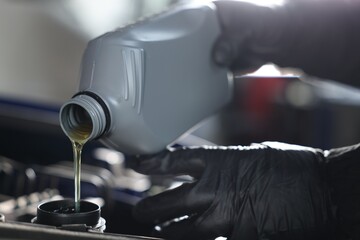 Worker pouring motor oil from canister into car engine, closeup