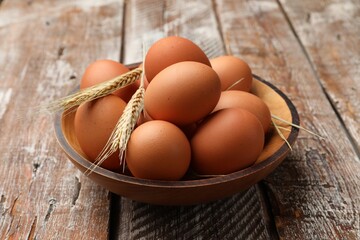 Raw eggs and spikes of wheat on wooden table, closeup