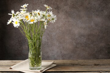 Many beautiful chamomile flowers in vase on wooden table against brown textured background,...