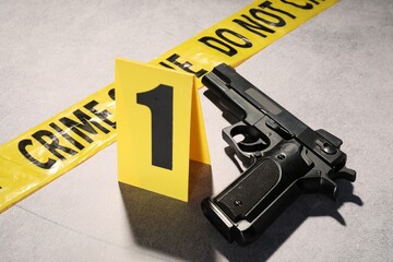 Forensic expertise. Crime scene tape and gun on light grey background, closeup