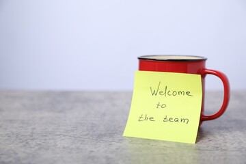 Sticky note with phrase Welcome To The Team and coffee on grey table, closeup. Space for text