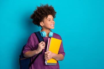 Smiling boy with curly hair holding notebooks against bright blue background, embodying trendy and...