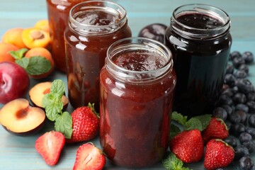 Different jams in jars and ingredients on blue wooden table, closeup