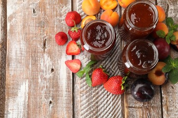 Different jams in jars and ingredients on wooden table, flat lay. Space for text