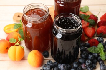 Different jams in jars and ingredients on white wooden table, closeup