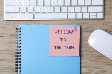 Paper note with phrase Welcome To The Team, keyboard and stationery on wooden table, flat lay