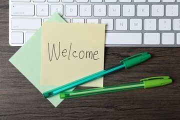 Paper note with word Welcome, pens and keyboard on wooden table, flat lay © New Africa