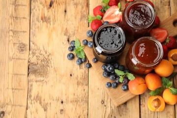 Different jams in jars and ingredients on wooden table, flat lay. Space for text