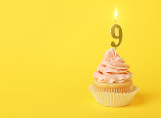 Yummy cupcake with burning golden candle in shape of number 9 on yellow background, space for text....