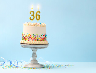 Yummy cake with sprinkles, burning number shaped candles on light blue background, space for text. 36th birthday or other special occasion