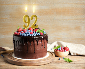 Yummy chocolate cake with berries and burning number shaped candles on wooden table, space for text. 92th birthday or other special occasion