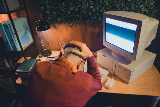 Senior man struggling with computer at home office, illustrating challenges with technology and work during retirement