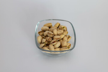 A clear glass bowl filled with salted pistachios placed on a clean white background. Healthy snack concept.