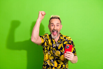 Excited middle aged man celebrating success with raised hand and smartphone on a vibrant green background