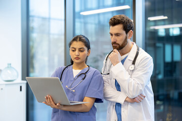 Two medical professionals, a doctor and a nurse, looking at a laptop screen, possibly discussing a...