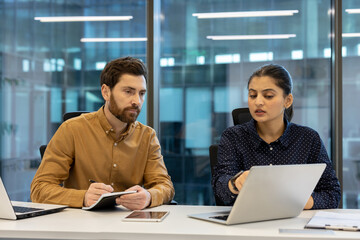 A business team collaborating in an office setting. They are focused on a laptop screen, discussing...
