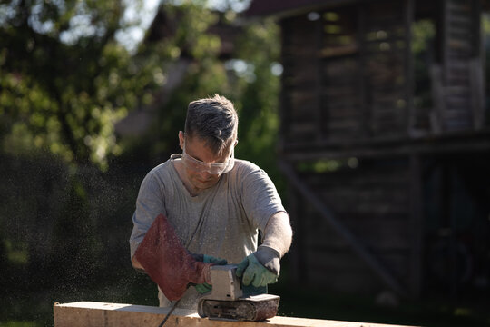 Carpenter sanding wood with belt sander in outdoor workshop