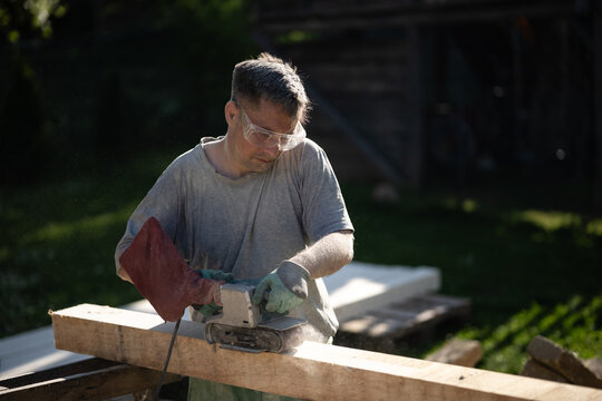 Carpenter sanding wooden beam with belt sander outdoors