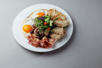 Healthy breakfast with eggs, bacon, grilled chicken, beans, salad and bread on white plate – top view gourmet morning meal on gray background