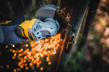 The hands of the master saw the metal with a grinder. Metal works in the workshop close up. Metal processing with angle grinder. Sparks in metalworking.