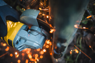 The hands of the master saw the metal with a grinder. Metal works in the workshop close up. Metal processing with angle grinder. Sparks in metalworking.