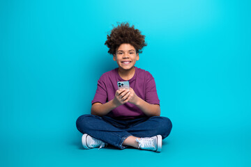 Charming young boy holding a phone smiles with happiness against a bright blue background