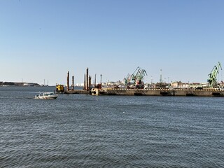 Klaipeda Harbour. Cranes dominate the industrial landscape of a harbor. Several green cranes stand along the dock, with some structures and machinery visible. 