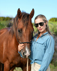 Fototapeta premium A young blonde woman smiling and cuddling with a brown horse