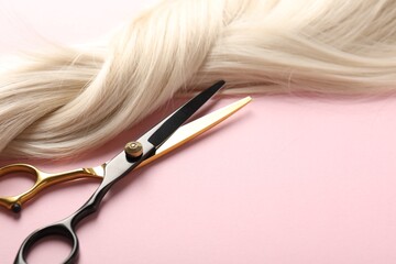 Hair strand and scissors on light pink background, closeup. Space for text