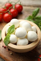 Tasty mozzarella cheese balls in bowl, basil, peppercorns and tomatoes on table, closeup