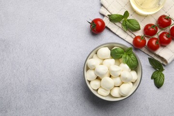 Tasty mozzarella cheese balls, tomatoes and basil on light grey table, flat lay. Space for text