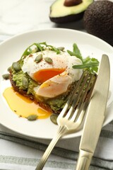 Delicious sandwich with avocado, poached egg, arugula and pumpkin served on table, closeup