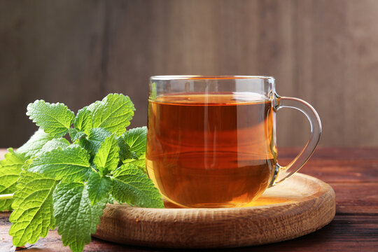 Aromatic lemon balm tea in glass cup and fresh leaves on wooden table, closeup