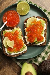 Delicious sandwiches with avocado, red caviar, cream cheese and lime on wooden table, flat lay